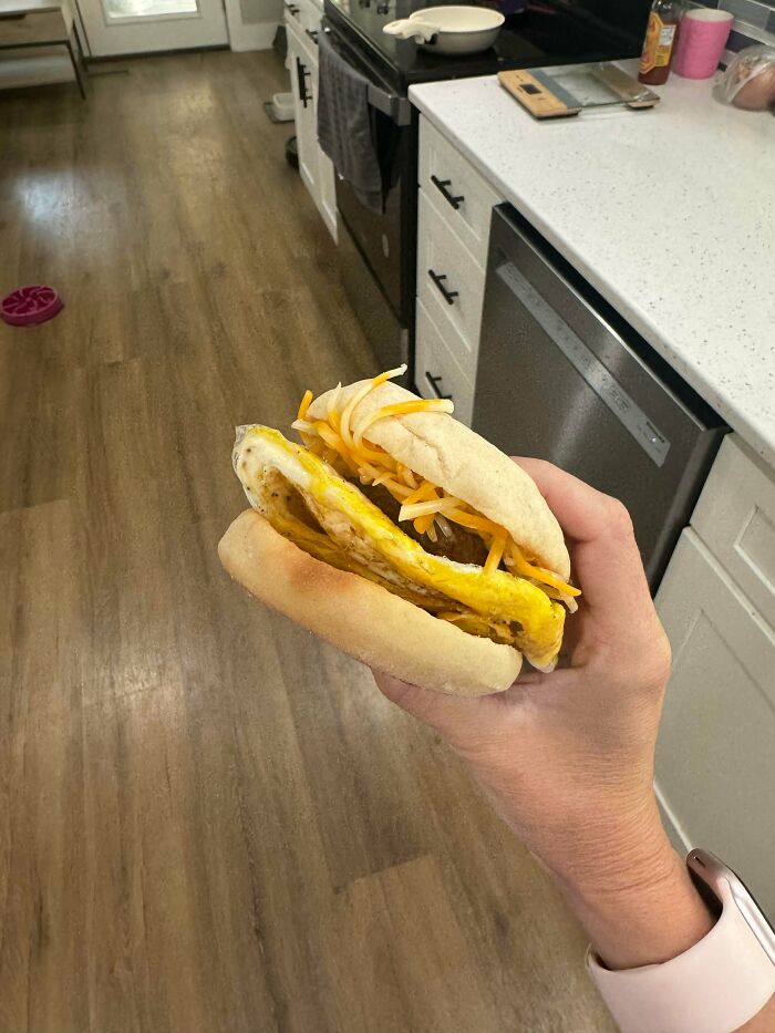 A hand holds an English muffin with egg and shredded cheese, a frugal tip for a new world economy.