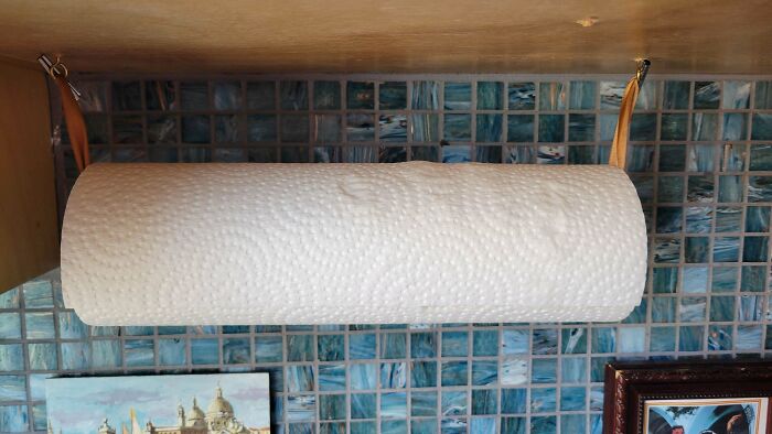 A roll of paper towels hangs under a cabinet, suspended by two leather straps, against a blue tile backsplash. A whole new world of frugal tips.