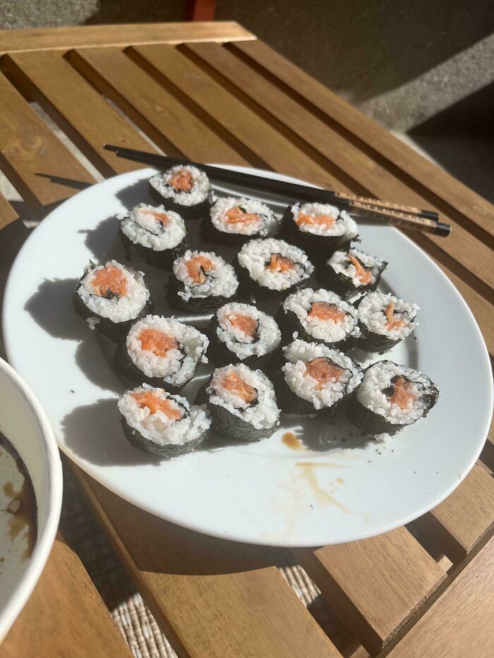 A white plate with salmon sushi rolls and chopsticks on a wooden table, representing frugal tips for a new world.