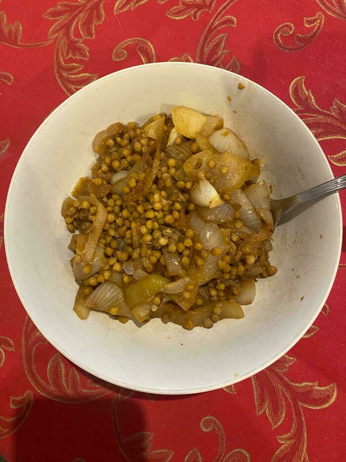 A white bowl of lentils and onions on a red tablecloth with gold patterns, representing frugal tips.