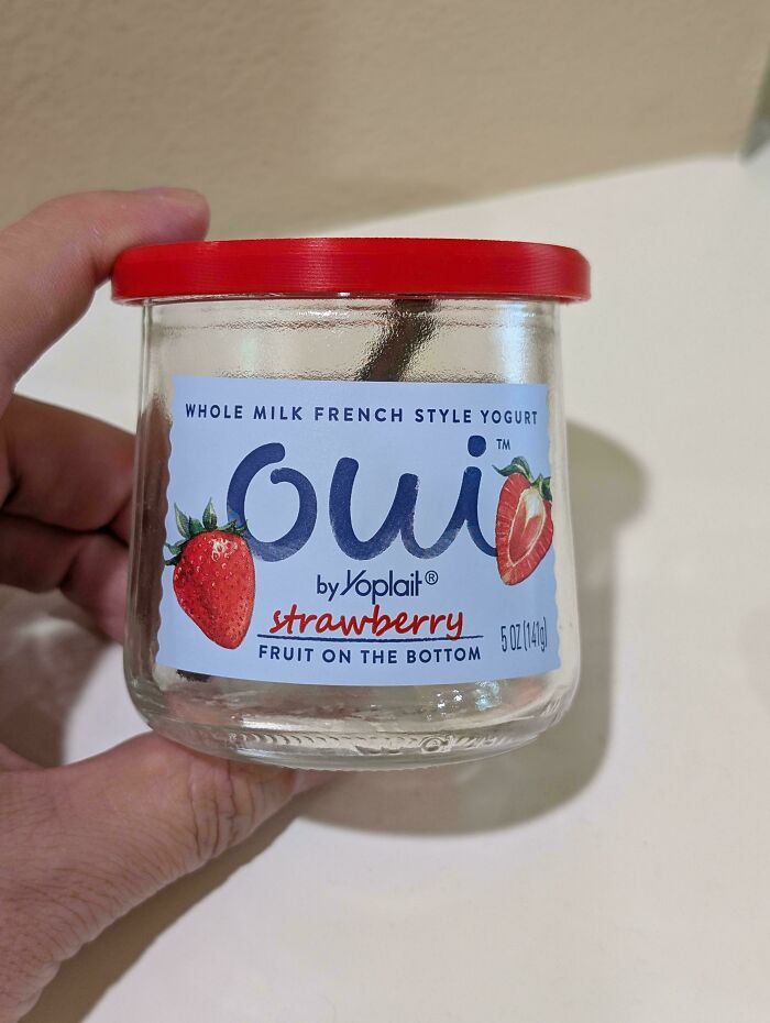 Hand holding a Oui by Yoplait strawberry yogurt jar with a red lid. A simple frugal tip for this economy.
