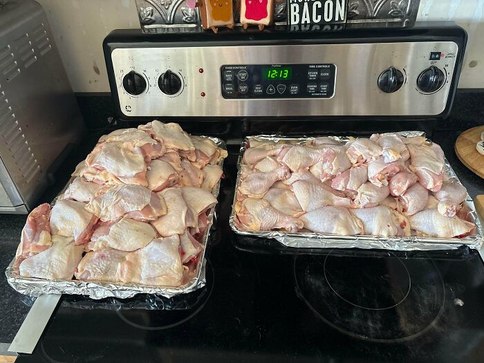 Two trays of raw chicken pieces on a stovetop, ready to be cooked, representing frugal tips in this economy.