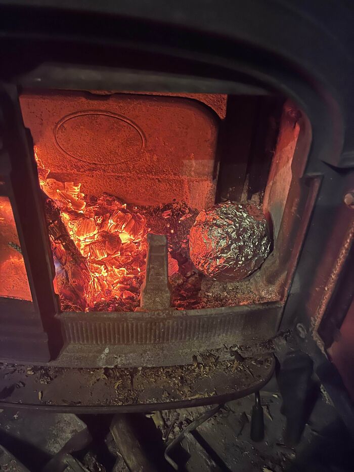 A foil-wrapped item cooking next to glowing embers in a wood stove, illustrating a frugal tip in this economy.