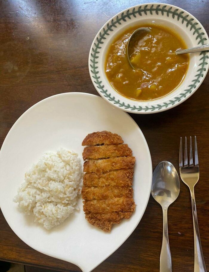 A plate of sliced katsu with white rice and a bowl of curry, reflecting a frugal meal.
