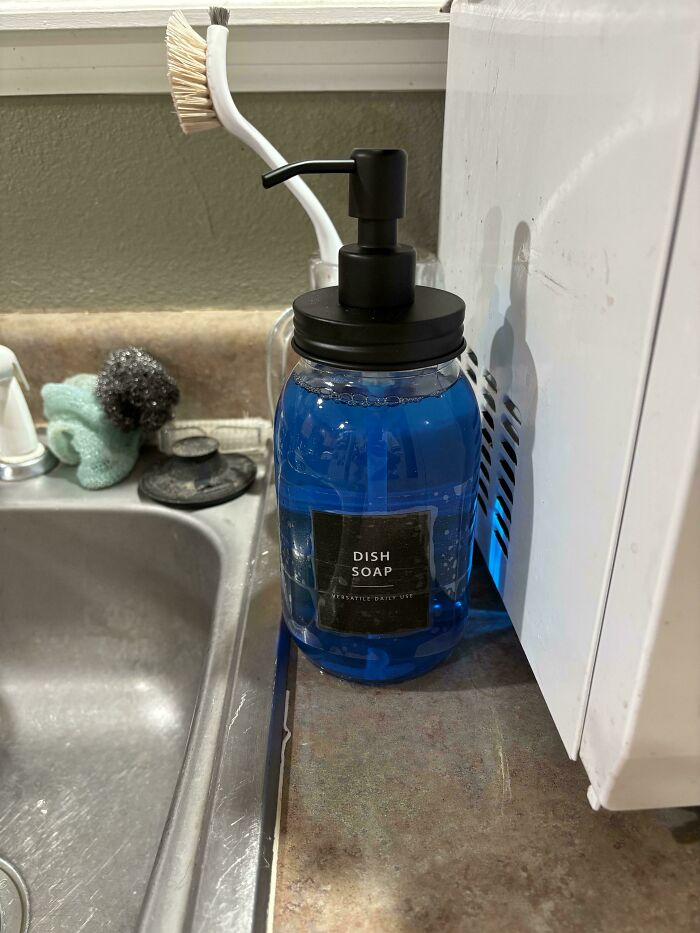 A frugal tip: a stylish dish soap dispenser on a kitchen counter next to a sink, with a dish brush in the background.