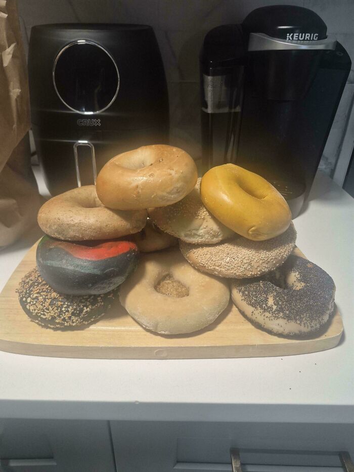 A pile of various bagels on a cutting board, with kitchen appliances in the background. Frugal tips for this economy.