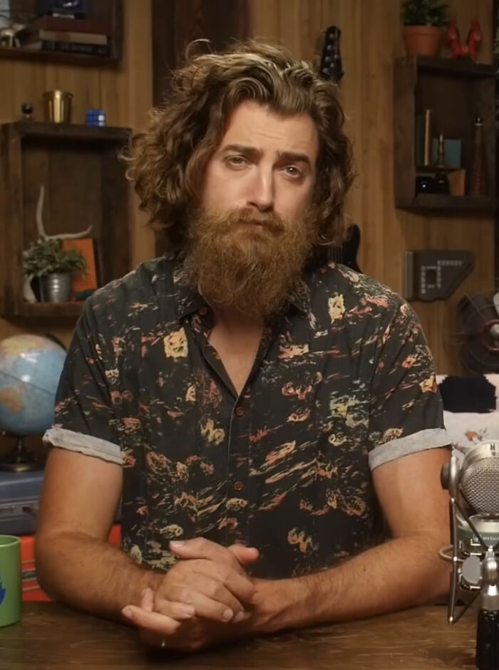 A man with amazing long hair and a beard, wearing a patterned shirt, with his hands clasped.
