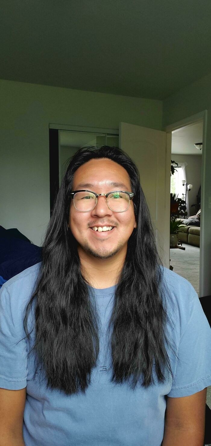 A man with amazing long hair, smiling, wearing glasses and a blue t-shirt.