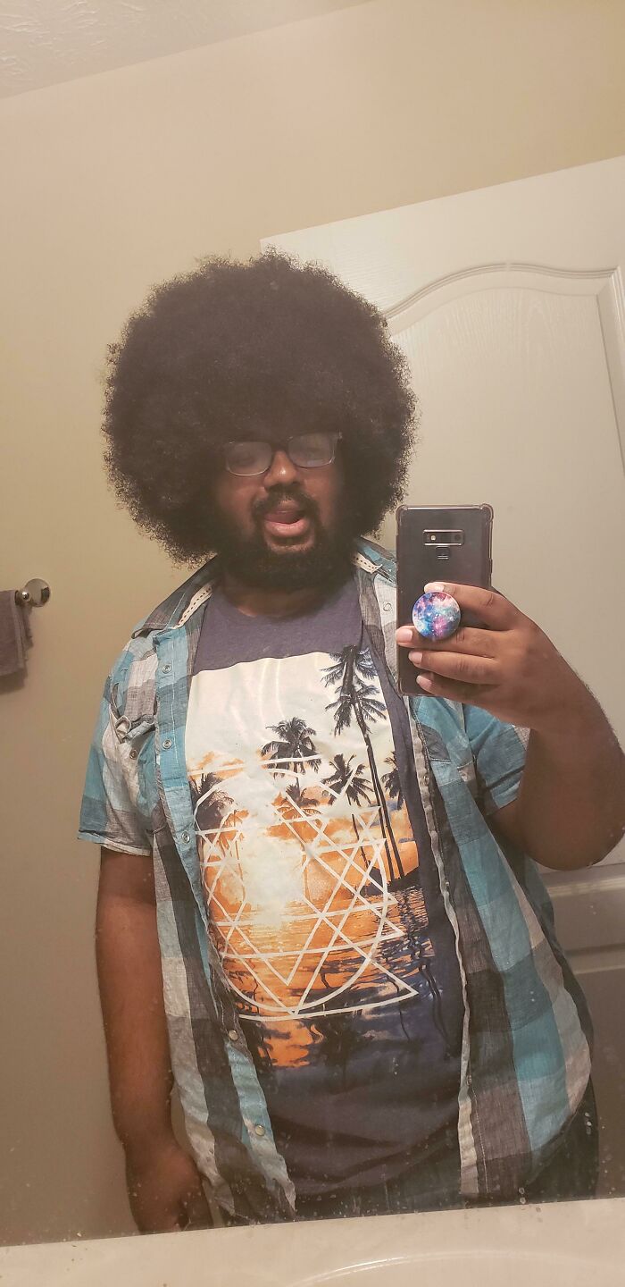 A man with a large afro, taking a mirror selfie, displaying his amazing long hair.