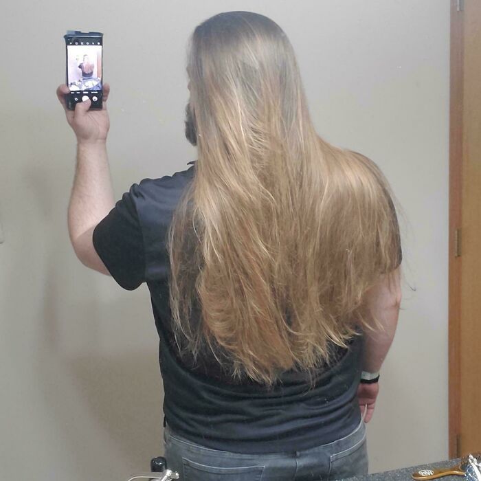 A man from behind, taking a selfie in a mirror, showcasing his very long hair.