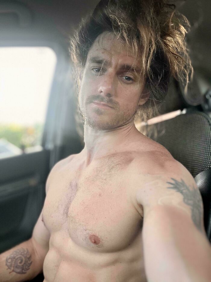 A man with messy long hair, sitting in a car, looking directly at the camera with amazing long hair.