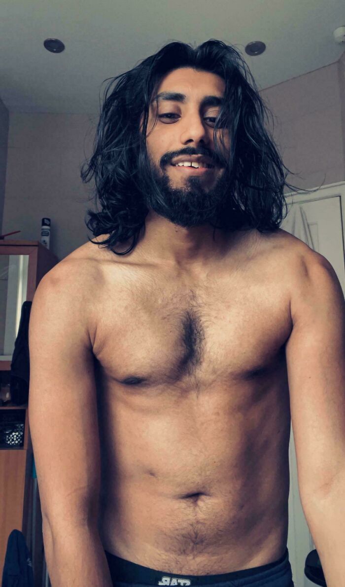 A smiling man with amazing long hair and a beard, standing shirtless indoors.