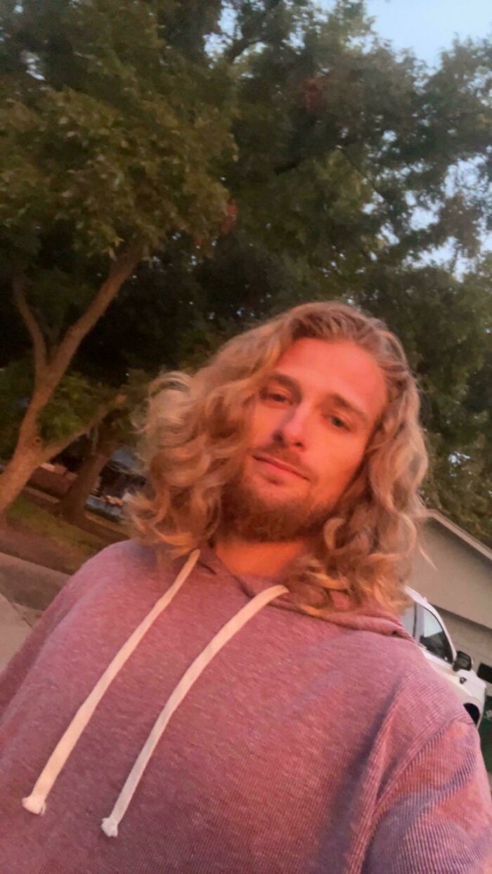 Handsome man with amazing long hair and a beard, smiling lightly outdoors.