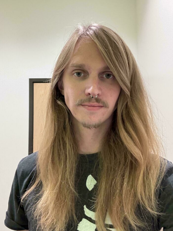 A man with amazing long hair and a subtle mustache and goatee, featuring a nose ring, in a neutral setting.