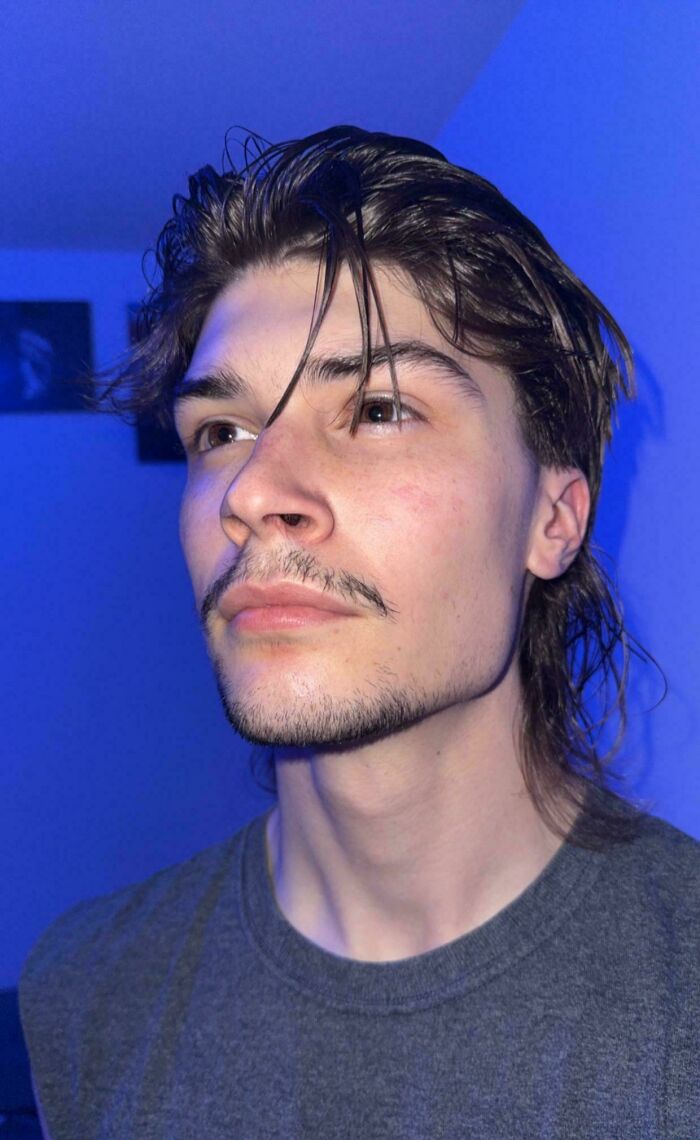A man with amazing long hair and a mustache, looking up and to the right against a blue background.
