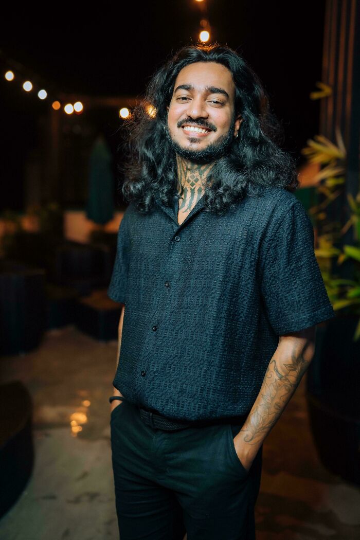 A smiling man with amazing long hair and a beard, wearing a black shirt, posing outdoors at night.
