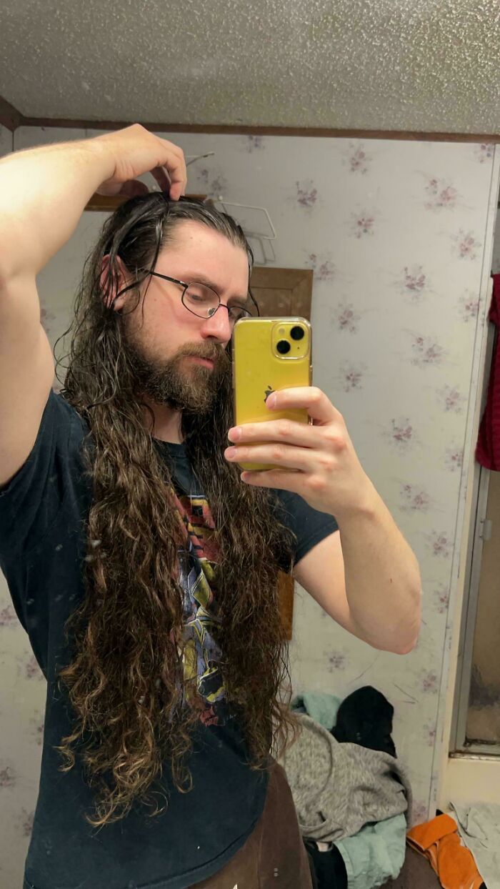 A man with ridiculously amazing long, curly hair and a beard takes a selfie in a mirror.