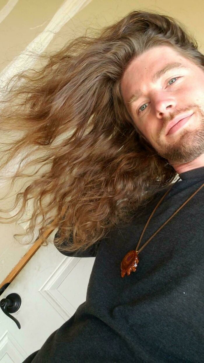 A man with amazing long hair flowing to the side, wearing a necklace and looking at the camera.