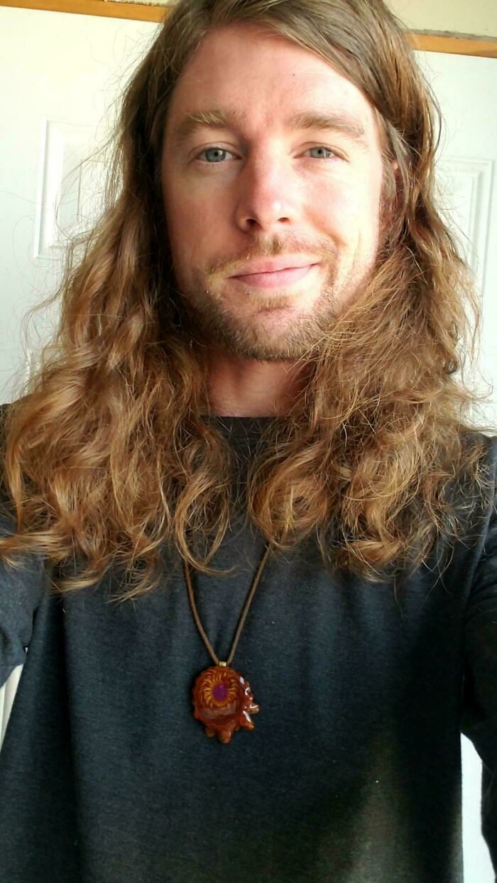 A man with amazing long hair smiling at the camera, wearing a necklace.