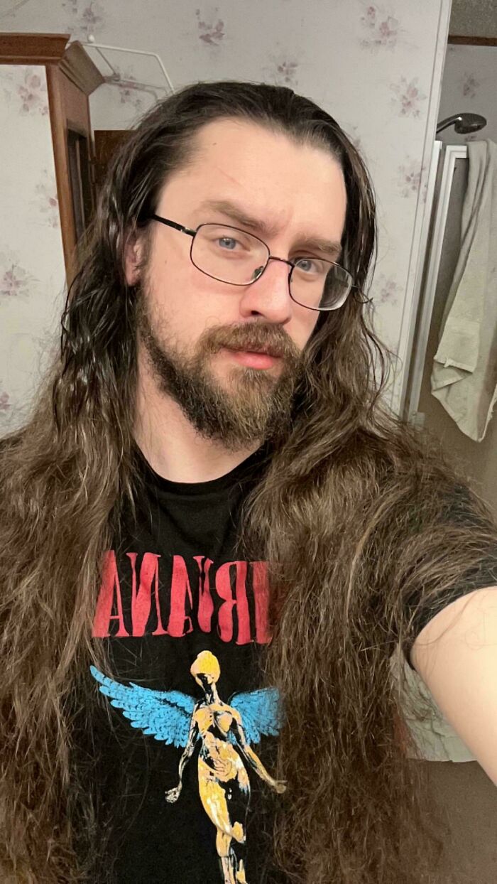A man with amazing long hair and a beard, wearing glasses and a Nirvana t-shirt.