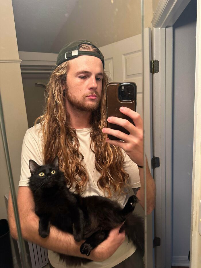 A man with amazing long hair and a cat, taking a selfie in a mirror.