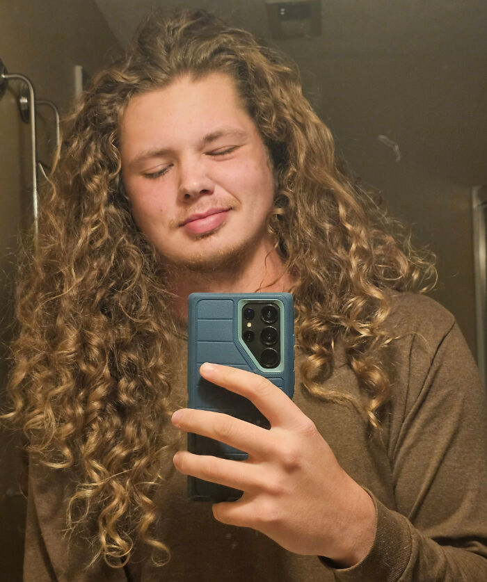 A man with incredibly long, curly, amazing hair taking a mirror selfie, eyes closed in enjoyment.