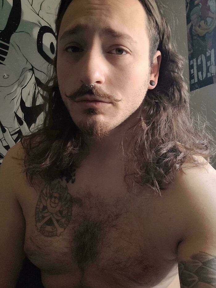 A man with amazing long hair, mustache, and nose ring, shirtless, with a tattoo on his chest.