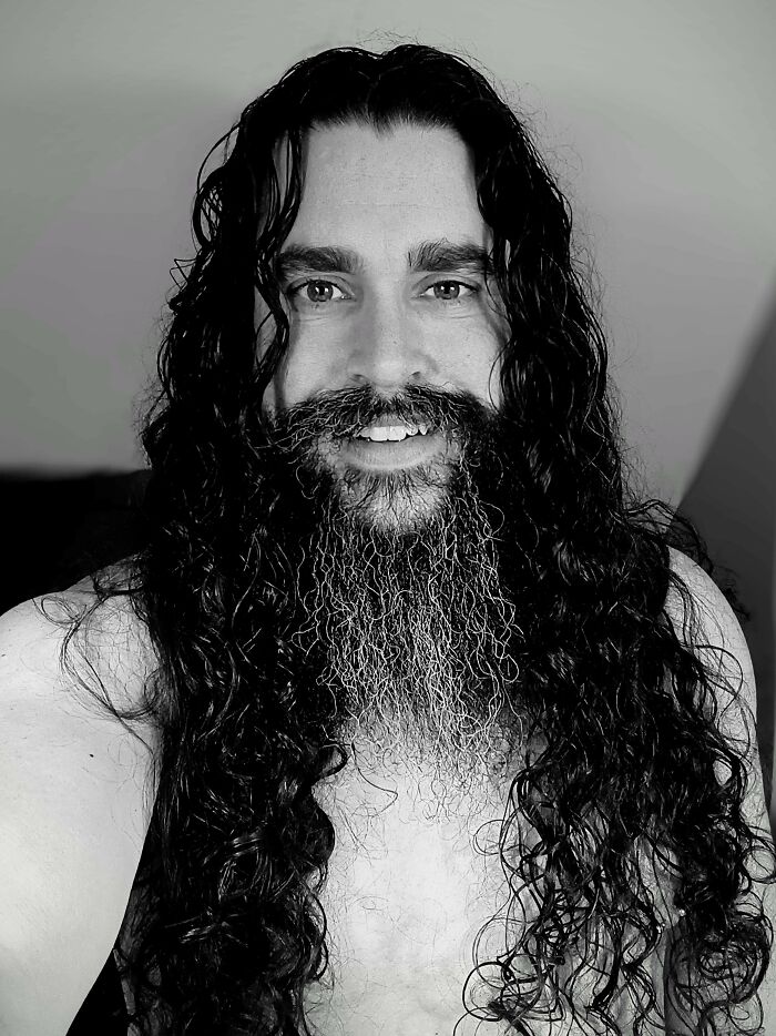 A man with amazing long hair, featuring very long dark curly hair and a long dark beard, smiling at the camera.