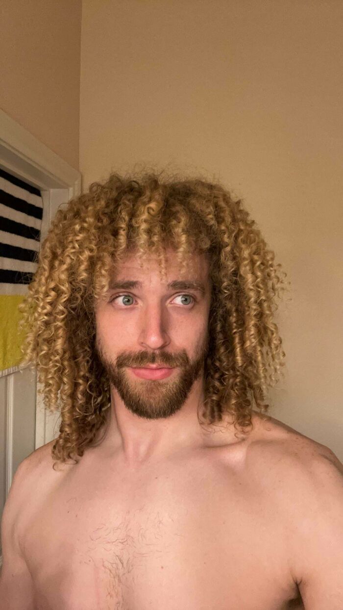 A man with amazing long hair, featuring a curly blonde afro, with a beard and mustache, looking to his right.