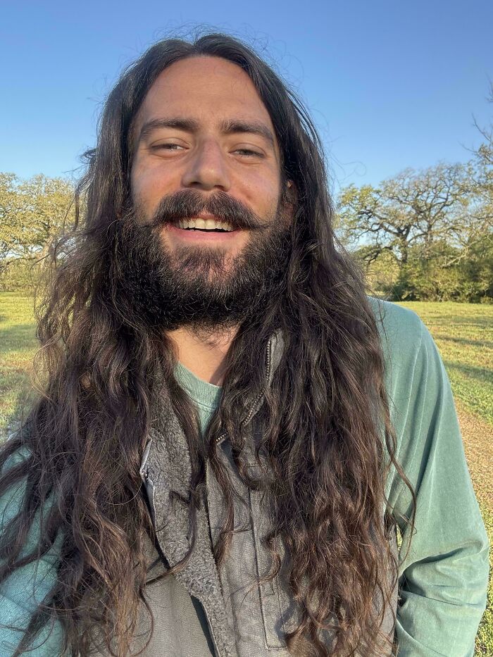 A smiling man with ridiculously amazing long hair and a beard stands outdoors.