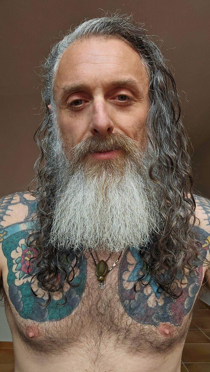 Close-up of a man with ridiculously amazing long hair, a long grey beard, and tattoos.