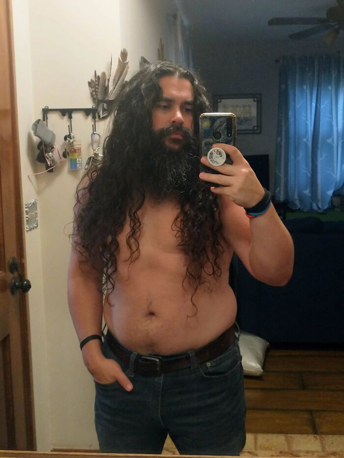 A man with ridiculously amazing long hair and a full beard takes a mirror selfie.
