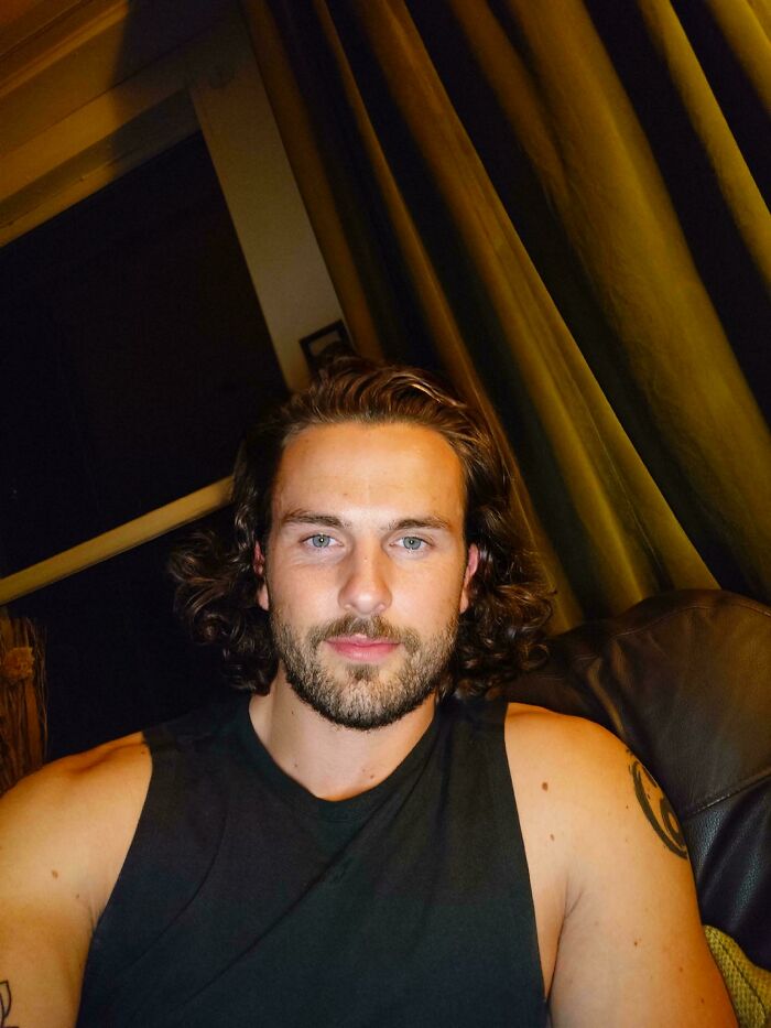 A man with amazing long hair and a beard, wearing a black tank top, with a tattoo on his arm.