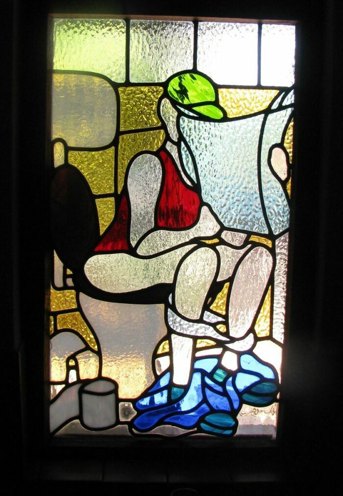 Stained glass window depicting a person sitting on toilet with newspaper showing craftsmanship wasted on weird concept