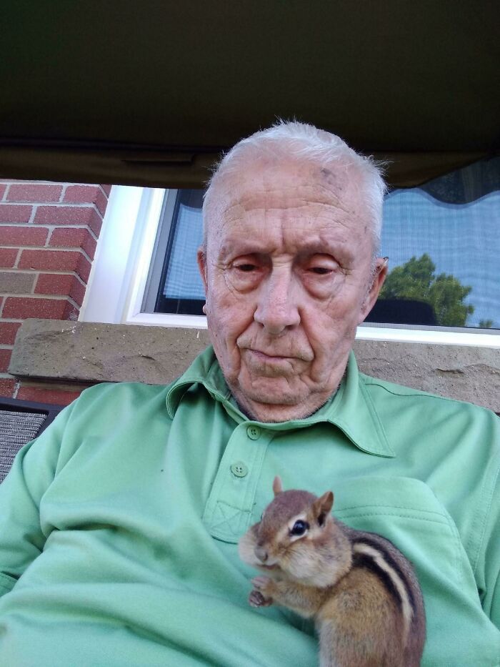 Elderly man in green shirt sitting outside with an adorable chipmunk on his chest lifting spirits with cute animal moment.