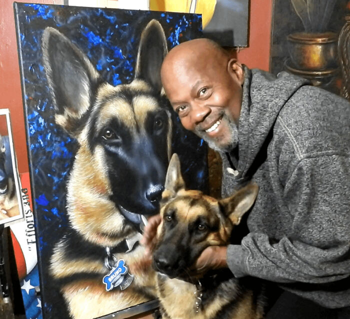 Man smiling and posing with a German Shepherd dog and its adorable painted portrait indoors.