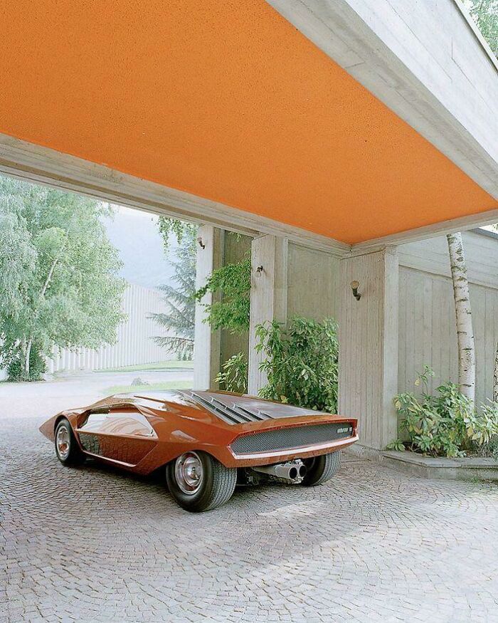 Orange retrofuturistic concept car parked under modern house overhang