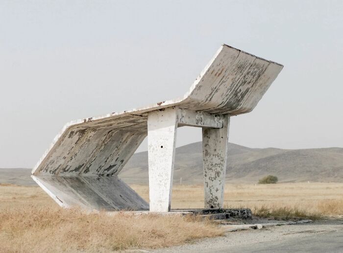 Retro brutalist bus stop shelter structure isolated in dry grassy field
