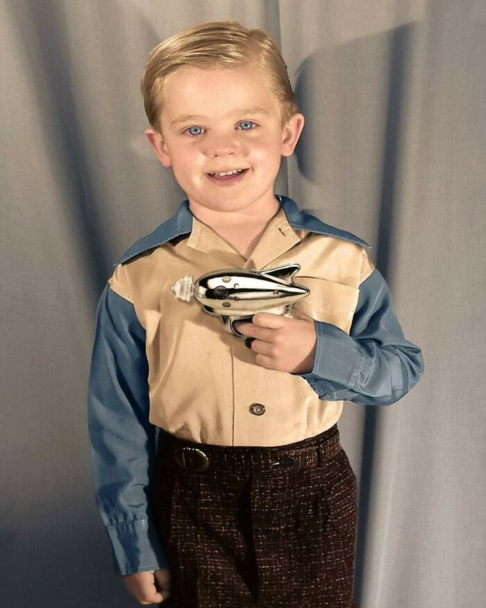 Young boy dressed in retrofuturism style holding a toy ray gun with a metallic finish