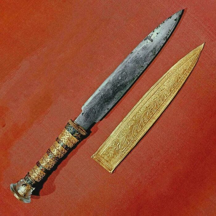An ancient golden dagger with intricate details lies beside its sheath, a striking historical photo.