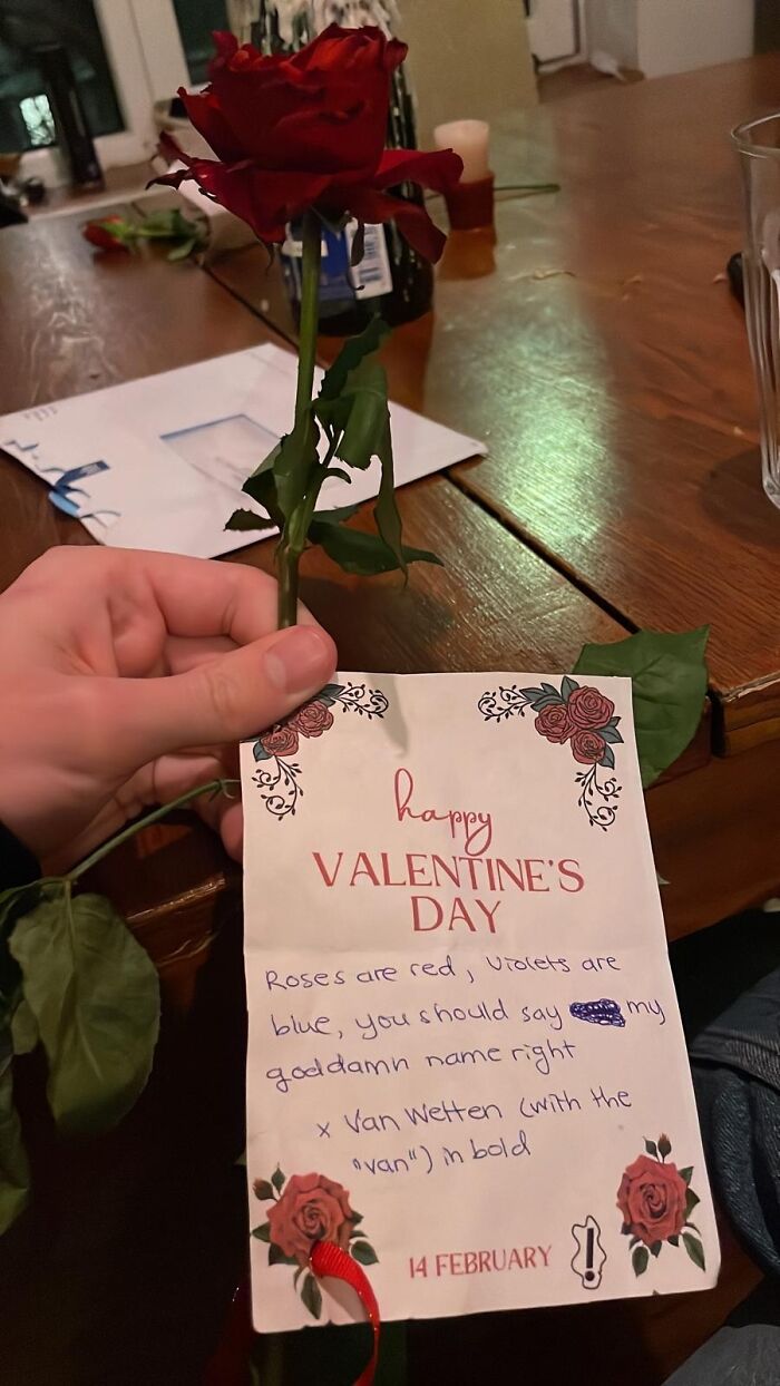 Hand holding a rose and a humorous Valentine’s Day card showing a failed attempt to understand instructions.