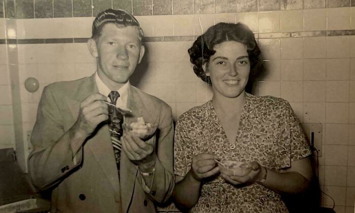 A couple smiling and eating dessert in an indoor setting, a candid old photo capturing moments from generations ago.