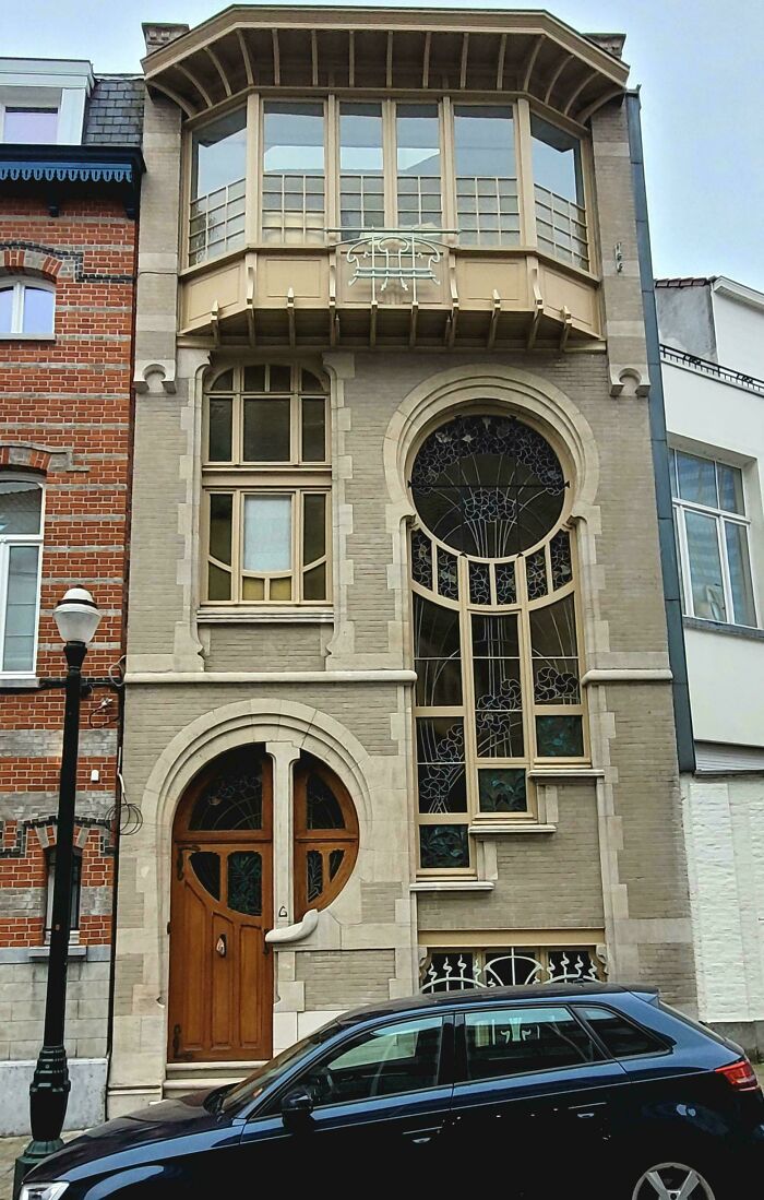 Unique and beautiful architecture of a building facade with an arched wooden door, large decorative windows, and a car in front.