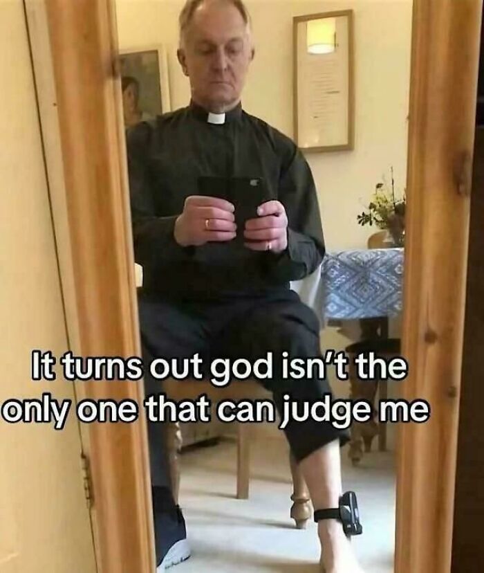 A priest in clerical attire looks in a mirror, holding a phone, with an ankle monitor visible, blending intelligentsia and foolishness.