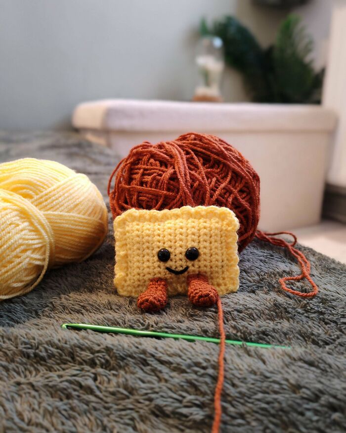 Crocheted smiling character with yarn balls and a green crochet hook on a textured gray surface showing DIY wins.
