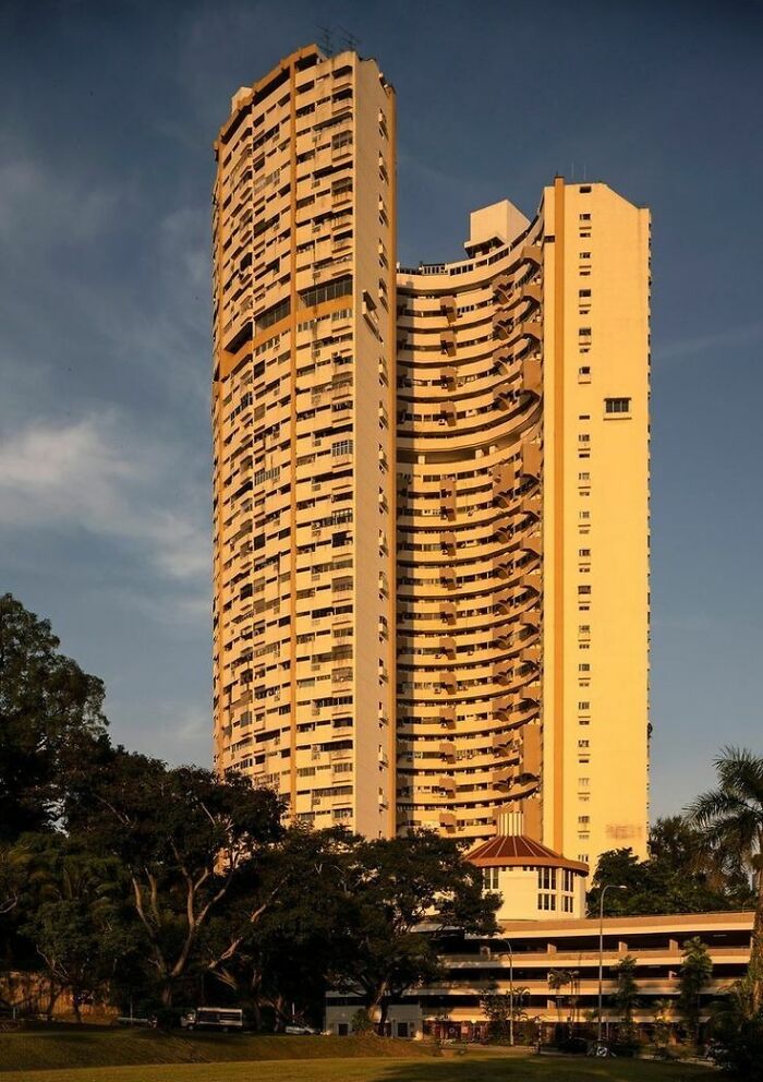 Tall interesting building with curved balconies standing against a clear sky, surrounded by trees and greenery.