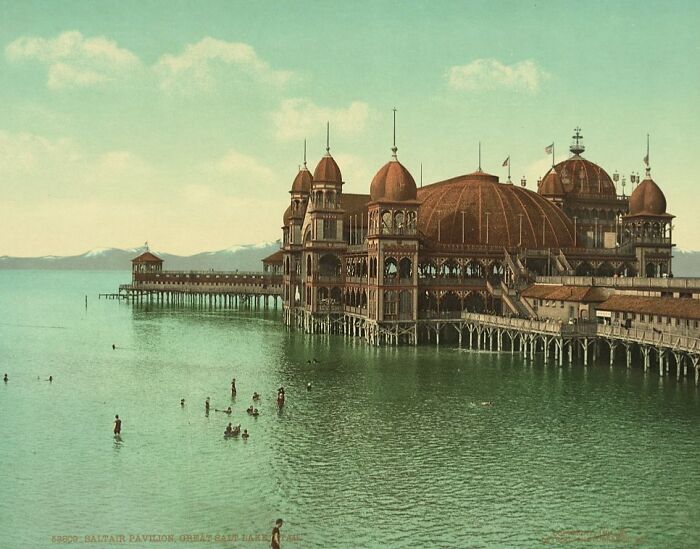 Historic interesting buildings over water with people swimming, showcasing unique architecture from a bygone era.
