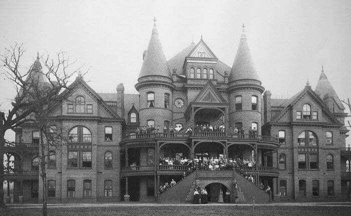 Historic Victorian building with turrets and crowds gathered on balconies, showcasing interesting buildings lost over time.
