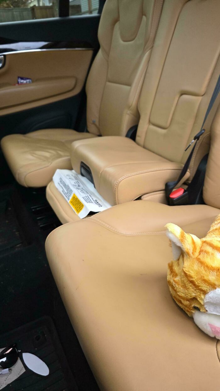 A great dad's car interior, featuring tan leather seats, a box between seats, and a stuffed cat toy.