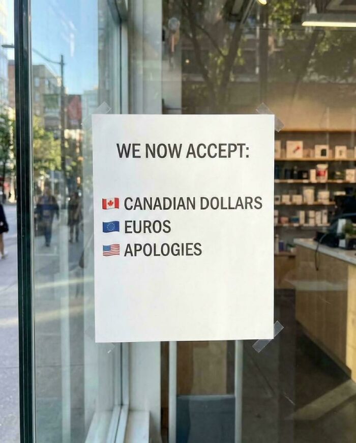 A sign on a glass door humorously states 'WE NOW ACCEPT: Canadian Dollars, Euros, Apologies,' a blend of intelligentsia and foolishness.